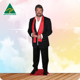 Cardboard standee of a man in a suit with a red sash on a wooden floor with a colorful background.